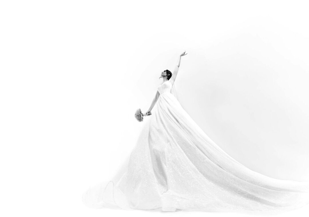 Bride in a modern minimalist wedding gown with a high sculptural ballerina bun, pearl accessories at the ears, sleek and polished, photograp