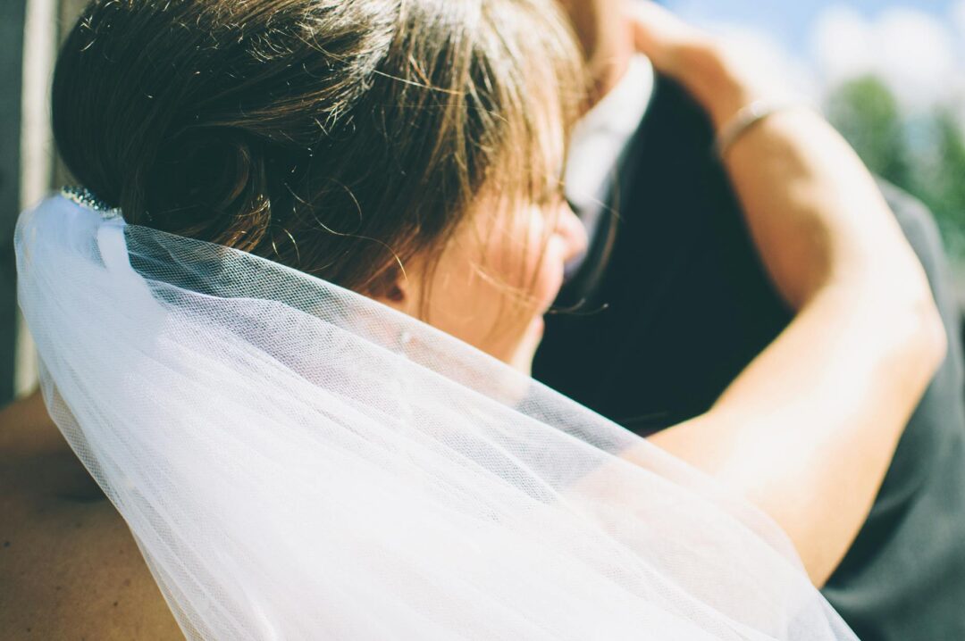 Bride with a bohemian low bun adorned with small dried florals and trailing eucalyptus sprigs, wearing an ethereal ivory gown, photographed