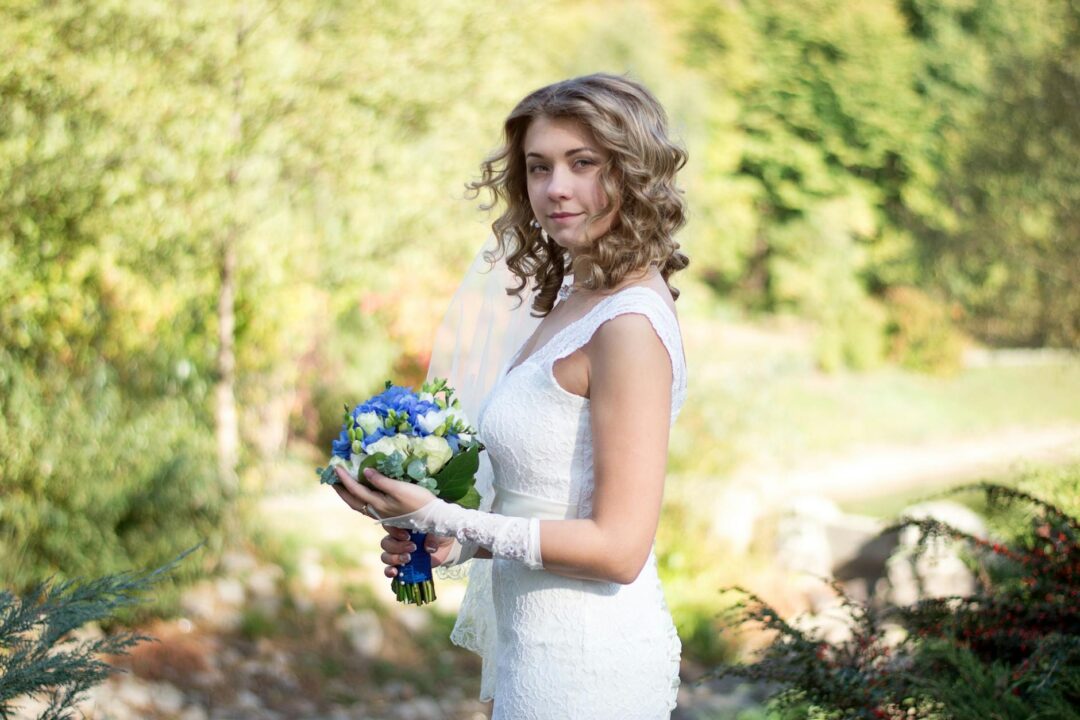 Bride with natural curly hair gathered into a low textured bun at the nape, soft curls visible in the bun body, a few loose ringlets framing