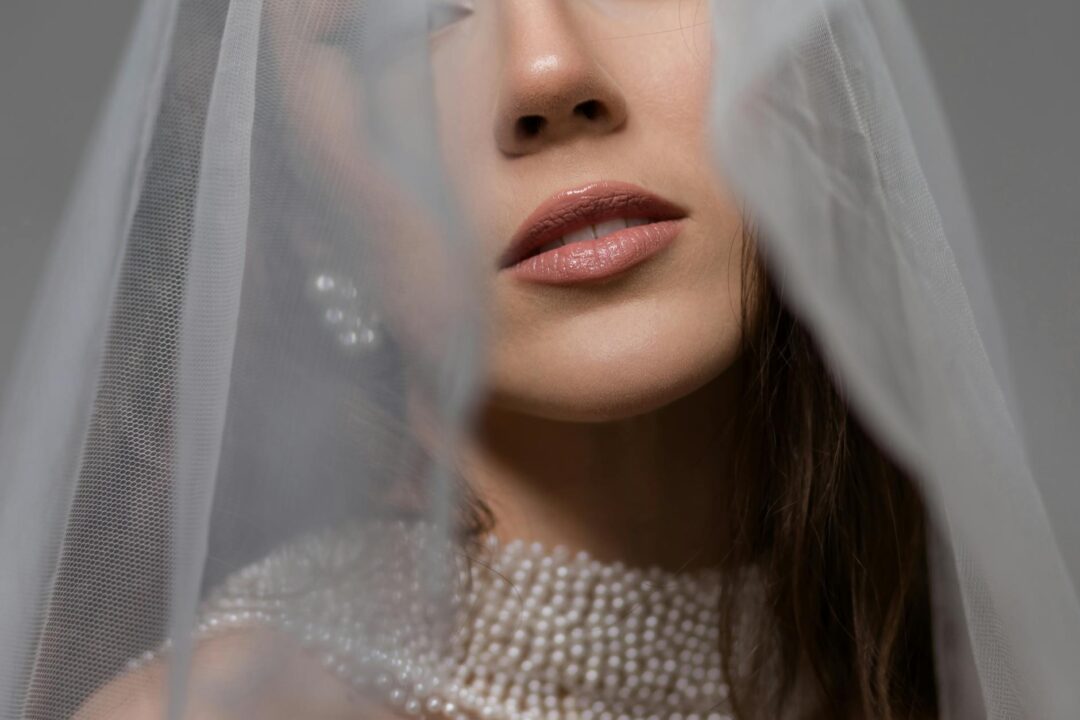 close-up bridal portrait of bride with a romantic low chignon adorned with a cluster of pearl-head pins and delicate face-framing tendrils, wearing a lace off-shoulder wedding gown, warm natural studi