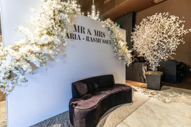 Elegant wedding photo booth backdrop with a white floral wall, Mr and Mrs signage, and a velvet lounge sofa