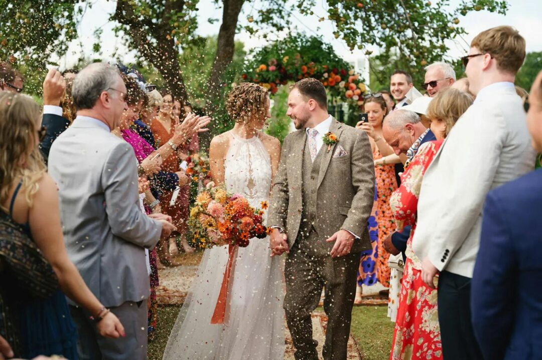 Wedding photographer directing a couple in an outdoor garden setting, couple laughing naturally while walking toward the camera