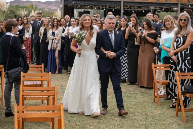 bride walking down aisle with father, wedding party assembled at front, soft natural light
