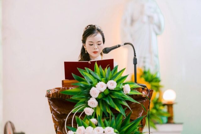 wedding reader at ceremony lectern, guests listening, sunlight through trees