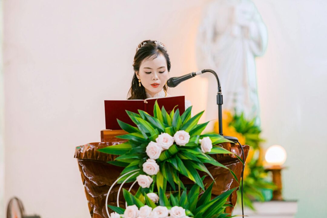 wedding reader at ceremony lectern, guests listening, sunlight through trees