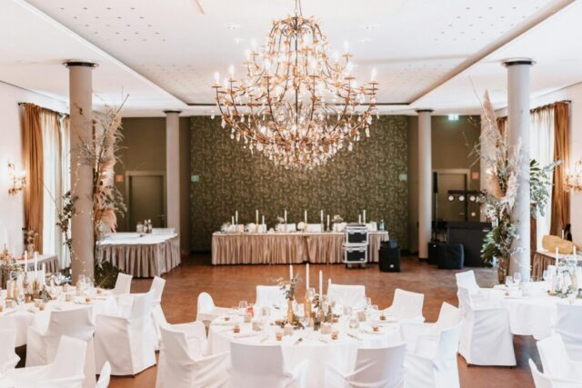Elegant wedding reception scene with guests seated at round tables raising champagne glasses during a toast, warm candlelight and floral cen