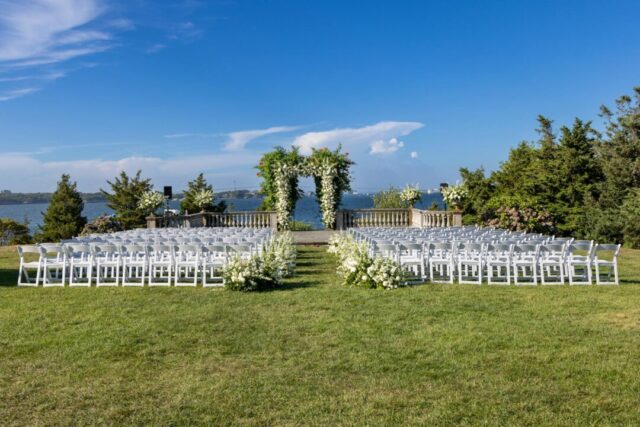 Elegant outdoor wedding ceremony setup with lush floral arch, warm golden light, and cream-colored chairs arranged in garden setting