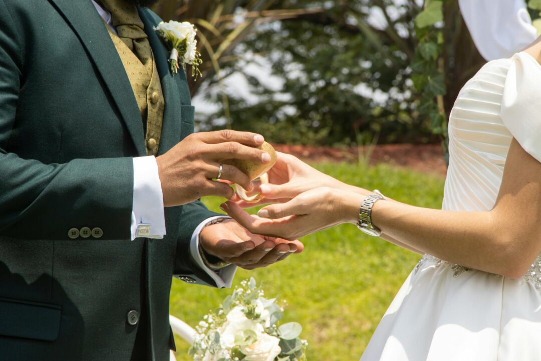 couple exchanging vows outdoors at a garden ceremony, officiant standing between them, guests seated in soft bokeh background