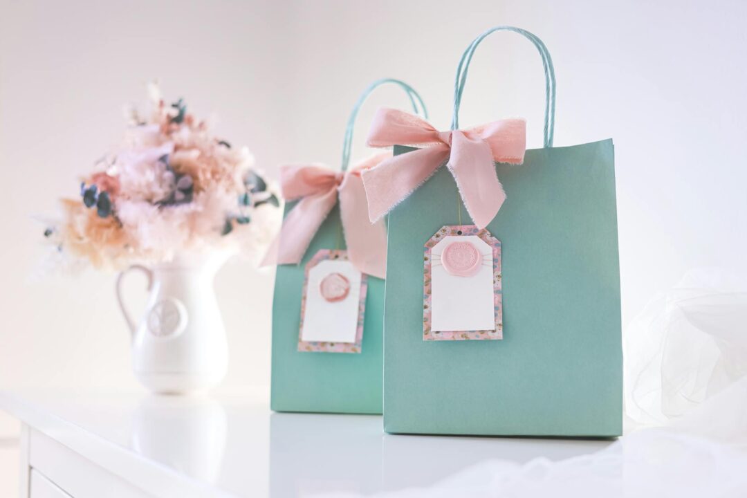 Paperlust gift bag tags with minimalist monogram 'A + J' design attached to kraft and white paper bags, soft natural lighting, showing how a