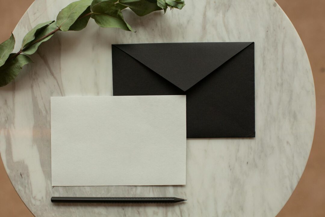 Elegant save the date card styled on a marble desk with an envelope and greenery, warm natural light, Paperlust product flatlay
