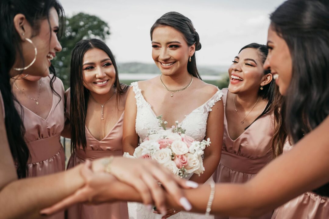 Four bridesmaids in matching dusty rose gowns walking together outdoors in natural light at a garden venue, laughing