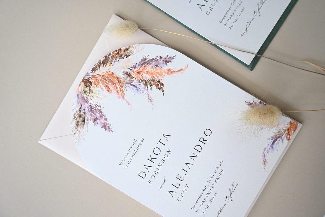 Paperlust invitation, Beautifully styled wedding invitation featuring pampas grass watercolor illustrations with dried floral props. The invitation lists a Texas venue