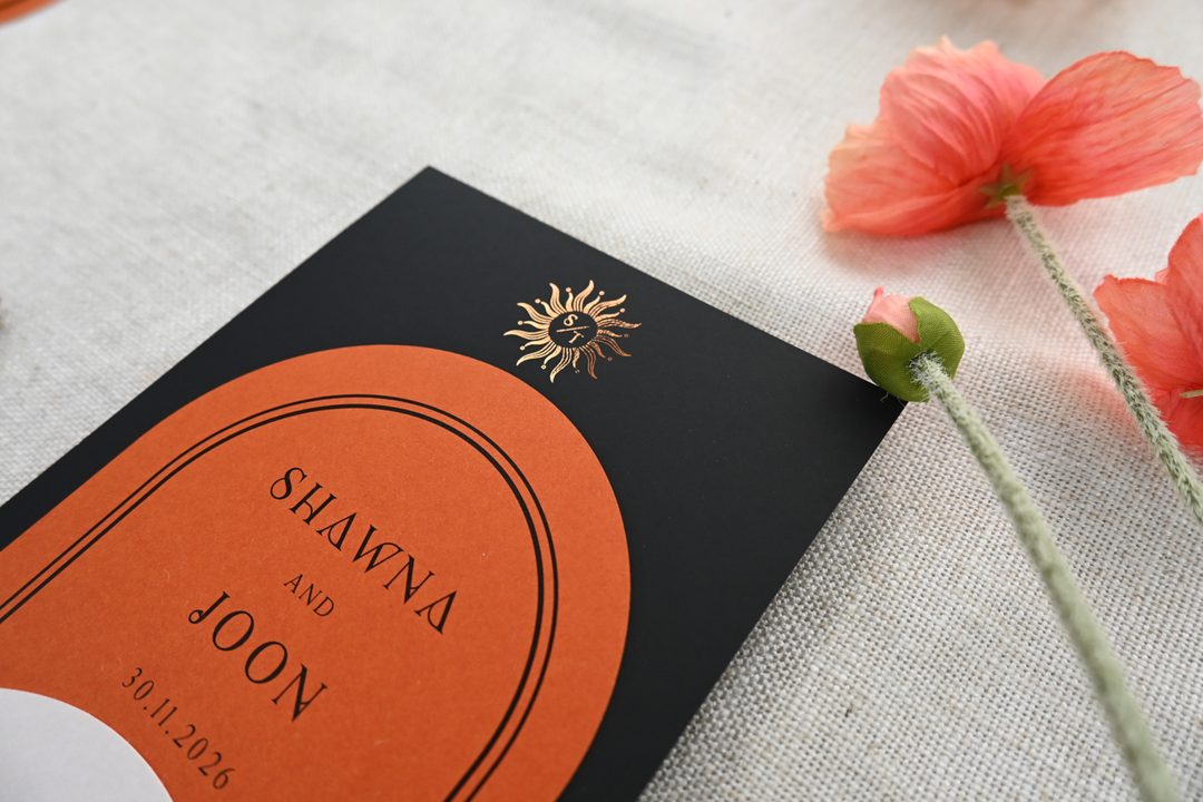 Paperlust invitation, Beautifully styled close-up of a black and burnt orange wedding invitation with gold foil sun motif