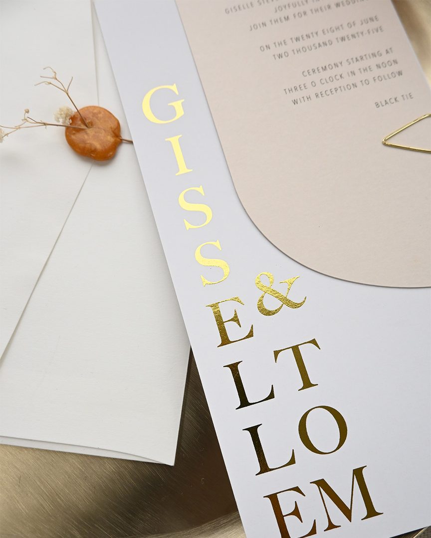 Paperlust invitation, Beautifully styled wedding invitation suite featuring gold foil typography on white stock with an elegant oval-shaped invitation card. The close-up angle highlights the luxe foil detail and premium paper quality.