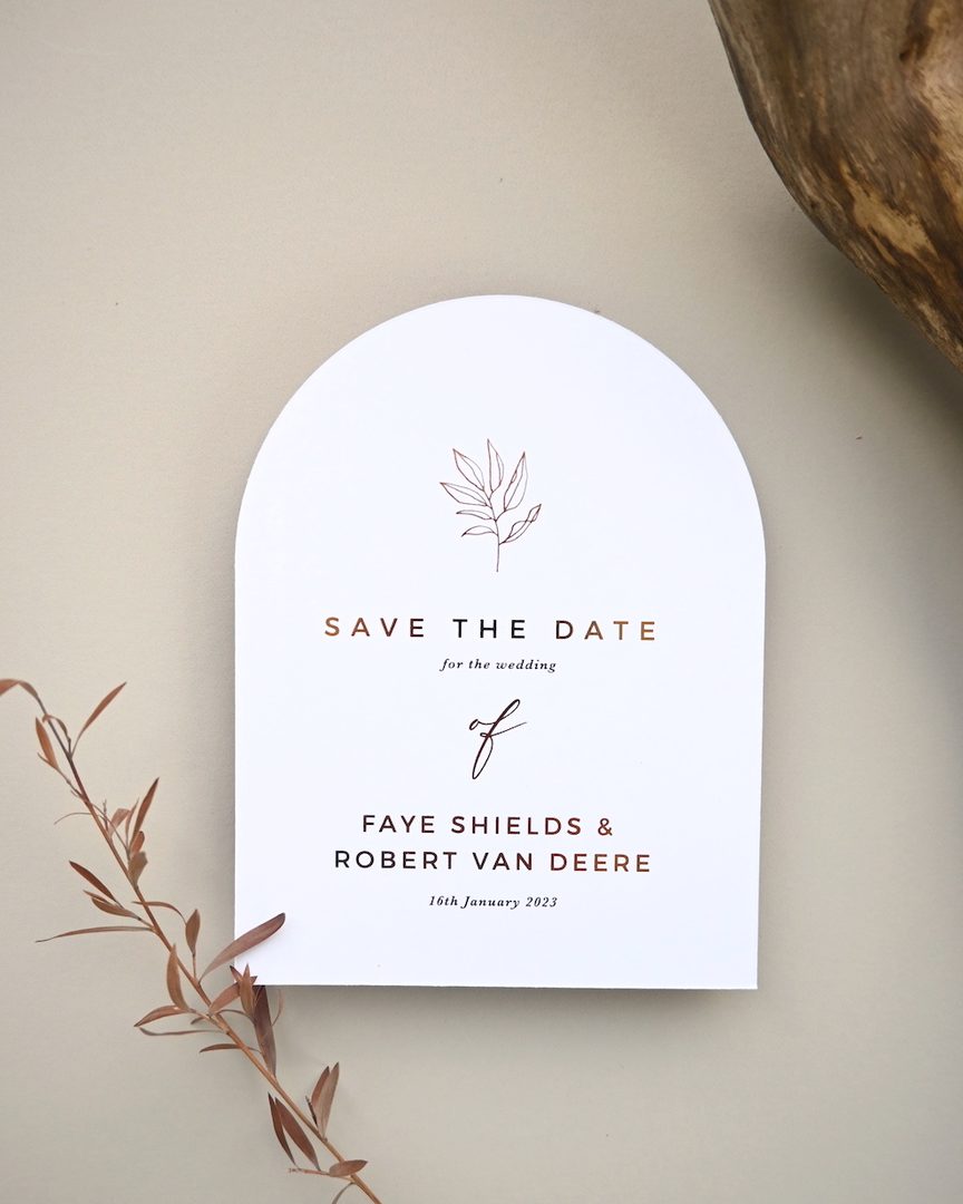 Paperlust invitation, Beautifully styled arch-shaped save the date card with elegant copper/bronze foil typography and a minimalist botanical motif