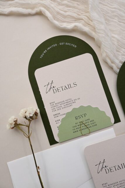 Paperlust invitation, Beautifully styled wedding stationery suite featuring arch-shaped dark green backing card with details card and RSVP piece. Elegant flatlay with dried flowers and soft fabric styling.