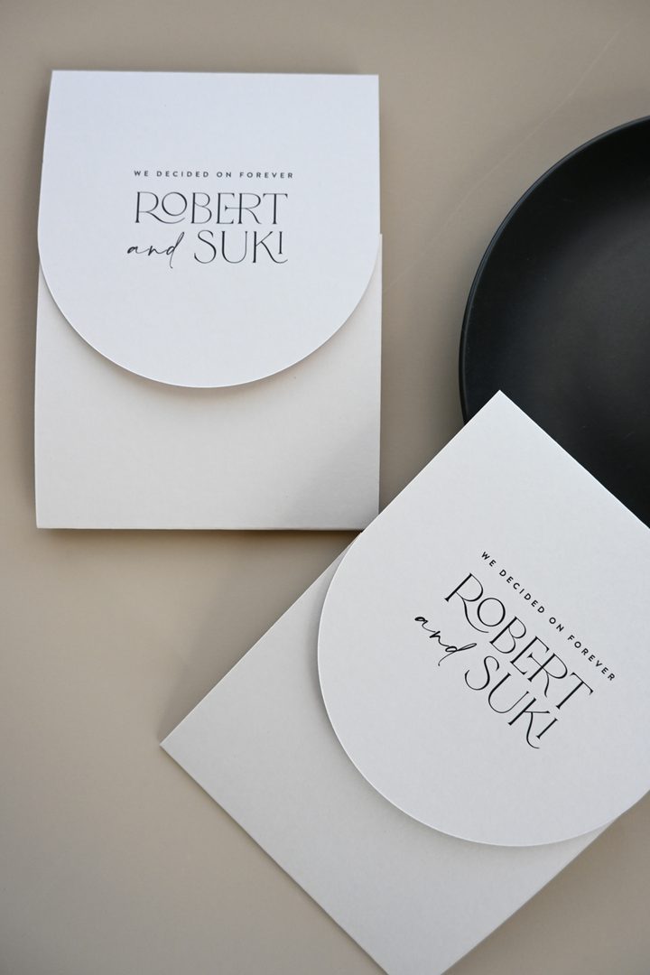 Paperlust invitation, Beautifully styled minimalist wedding invitation suite featuring elegant typography with a unique rounded flap envelope design. Clean neutral palette with strong visual appeal and professional lighting.