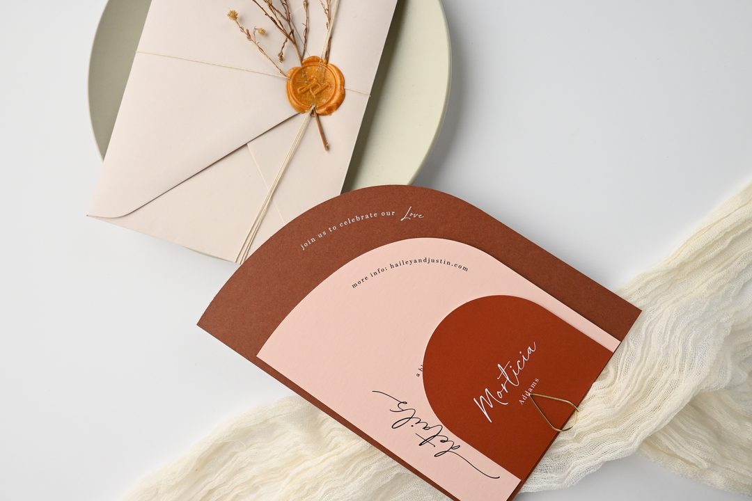 Paperlust invitation, Beautifully styled flatlay featuring an arch-shaped wedding invitation in warm terracotta and blush tones with a wax-sealed envelope
