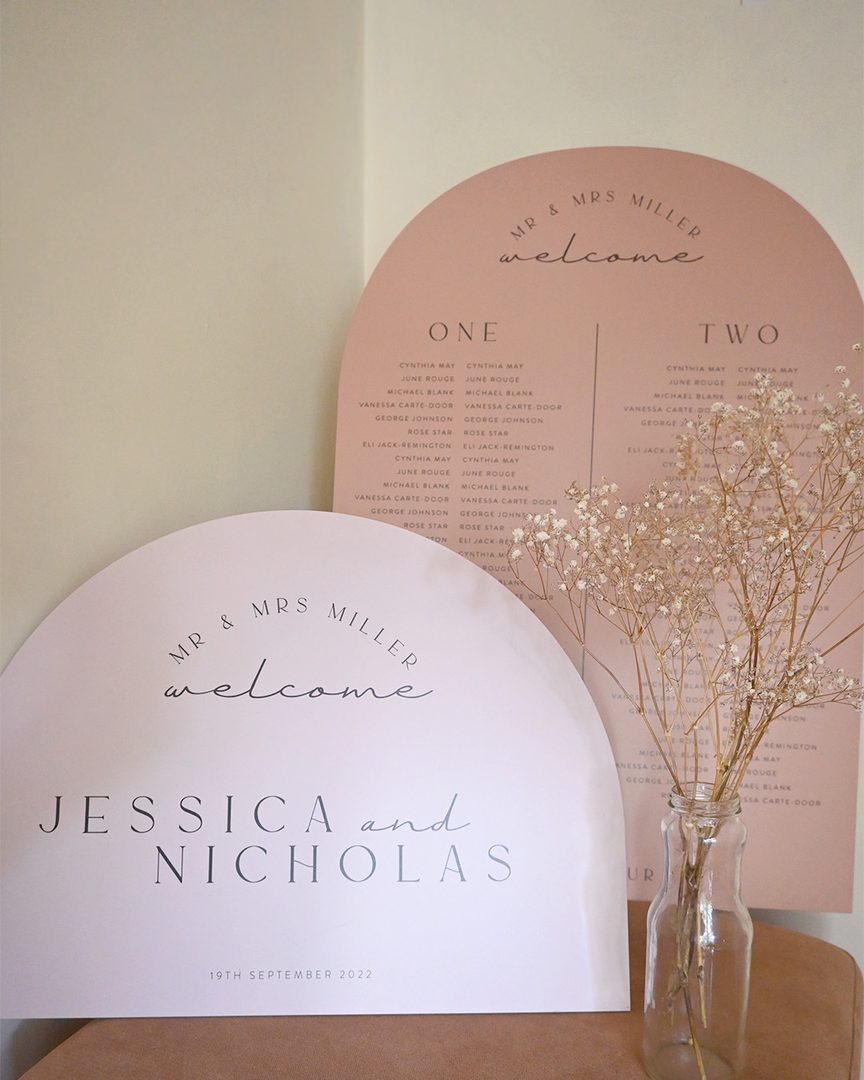 Paperlust seating chart, Styled display of arch-shaped wedding welcome sign and seating chart in blush/dusty rose tones with baby's breath accent. Good composition with warm