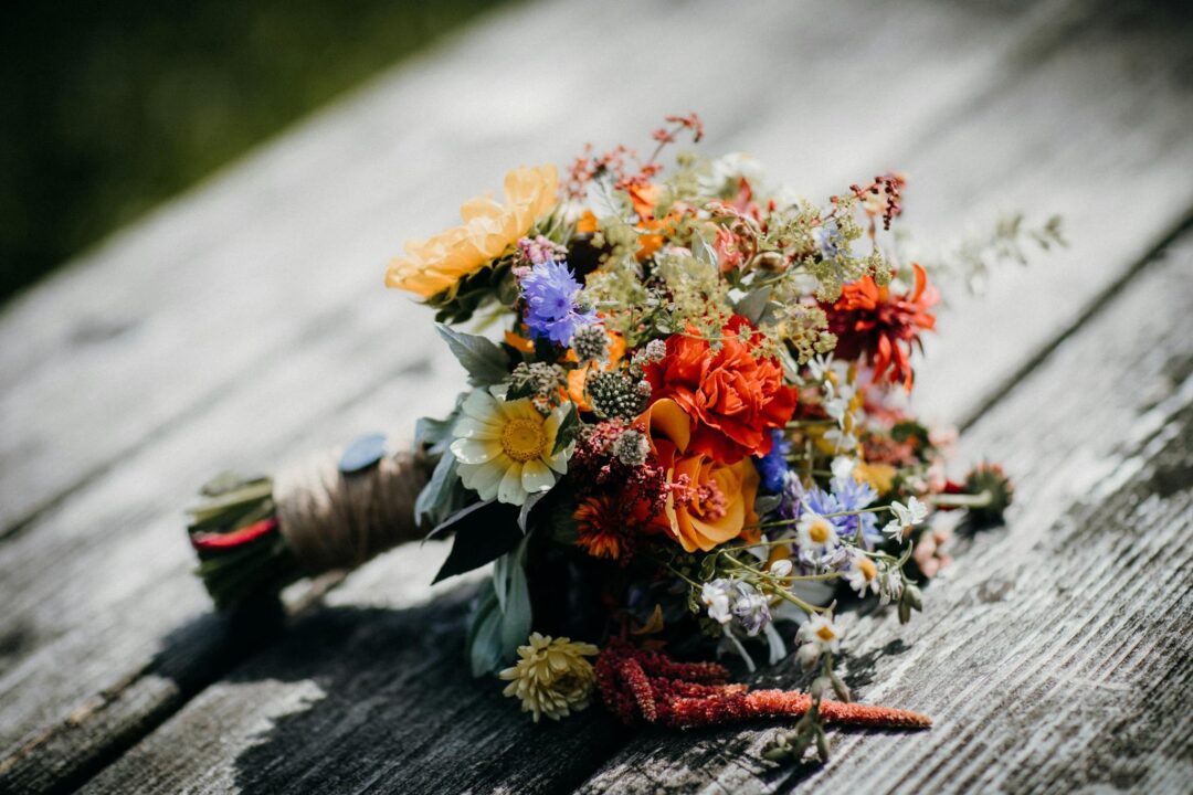 Vibrant locally-sourced wildflower bouquet wrapped in twine resting on a rustic weathered wooden surface, the seasonal, foraged bouquet aesthetic at the heart of sustainable wedding florals. Photo: Rene Terp / Pexels