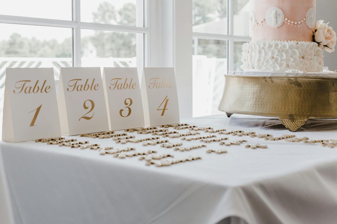 A champagne and gold wedding tablescape with ivory linen, gold candle holders, white garden roses, and eucalyptus greenery in low centerpiec