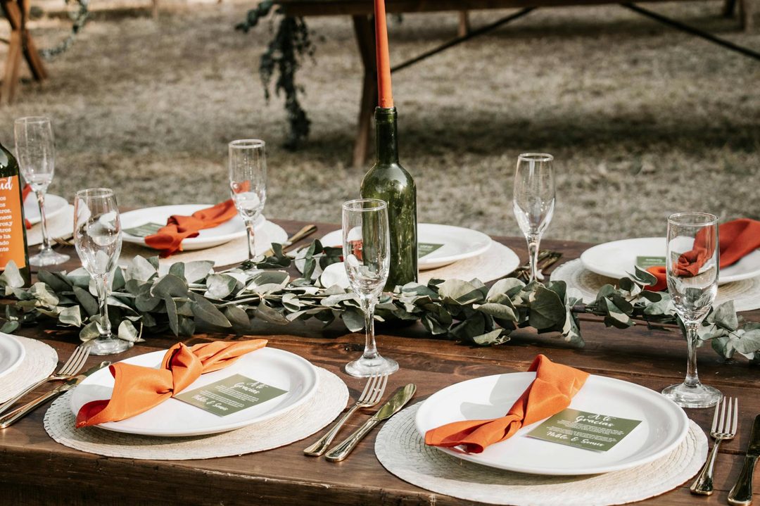 Styled reception table in burnt orange and sage with eucalyptus garland, amber glass vases, tapered candles, and cream linen tablecloth show