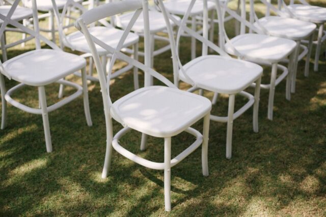 Wide sunlit outdoor wedding ceremony from above with rows of white chairs and a full crowd of guests, aerial perspective,...