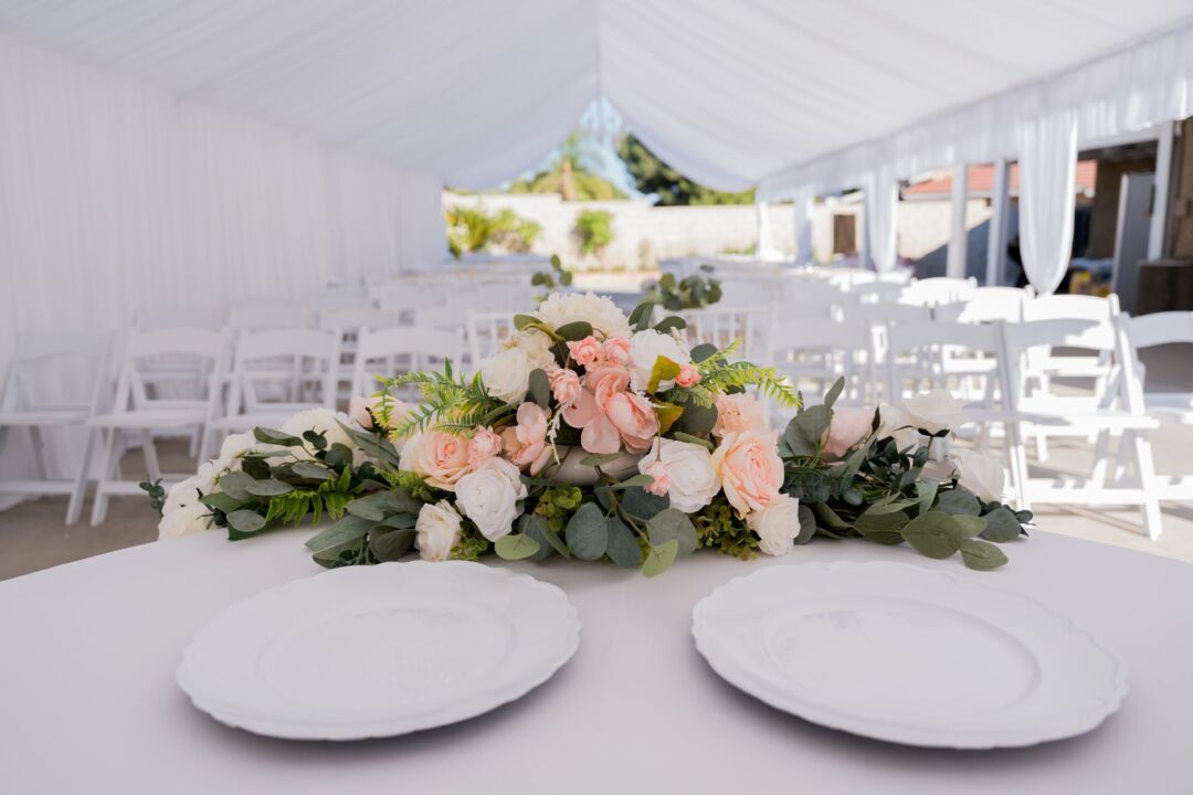 White peaked marquee tent erected in a suburban backyard for a wedding reception, string lights visible inside, round...