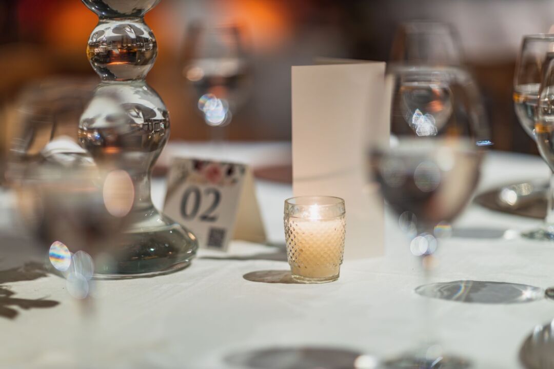 Small intimate restaurant table set for six with candles and a simple floral centerpiece, celebration dinner after a...