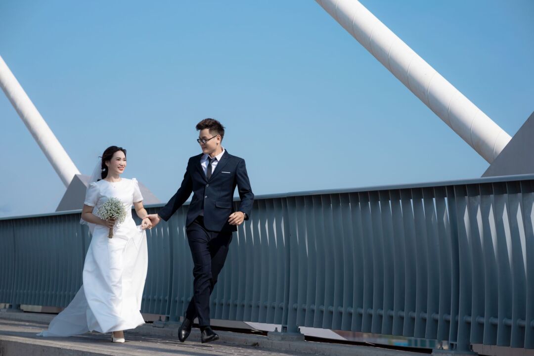 Smiling couple in simple modern attire holding a small bouquet on the marble steps of a city courthouse, candid...