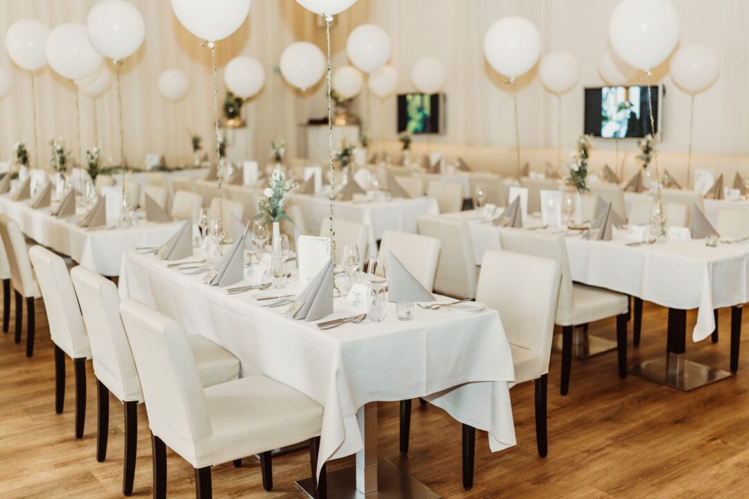 Seated family-style rehearsal dinner at a warm mid-range restaurant, guests passing large serving platters of pasta and...
