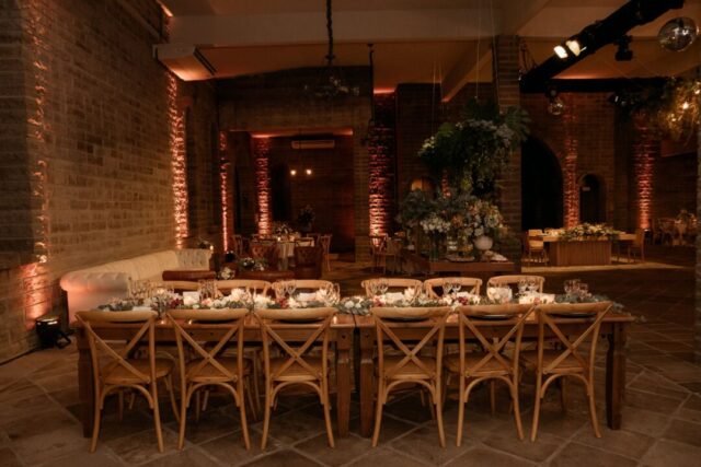Warm rehearsal dinner scene at a long candlelit table in a private restaurant dining room, the bridal party and close...