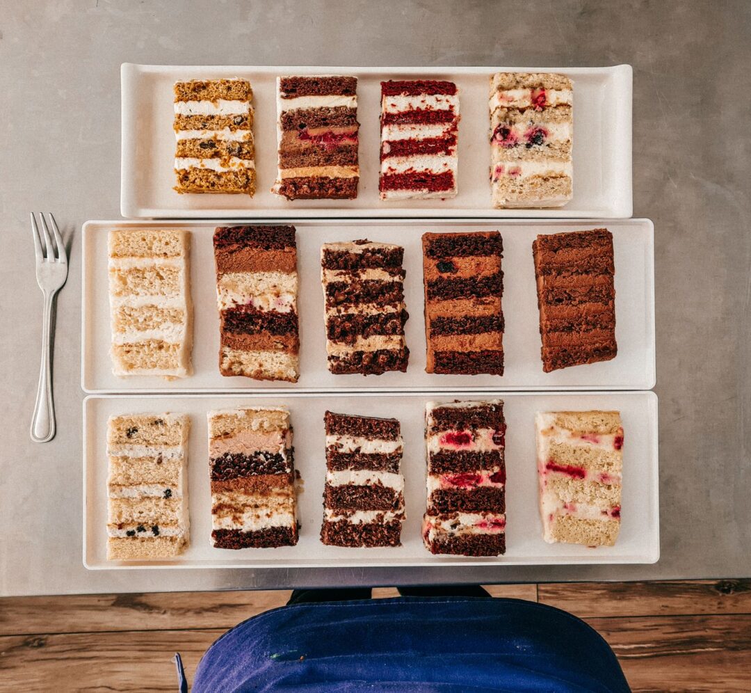 Wedding cake consultation at a bakery tasting table with small plates of three cake flavor samples, swatches of fondant...