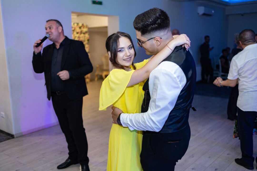 Wedding DJ performing at an indoor reception with colorful uplighting on a full dance floor, mixing equipment and...