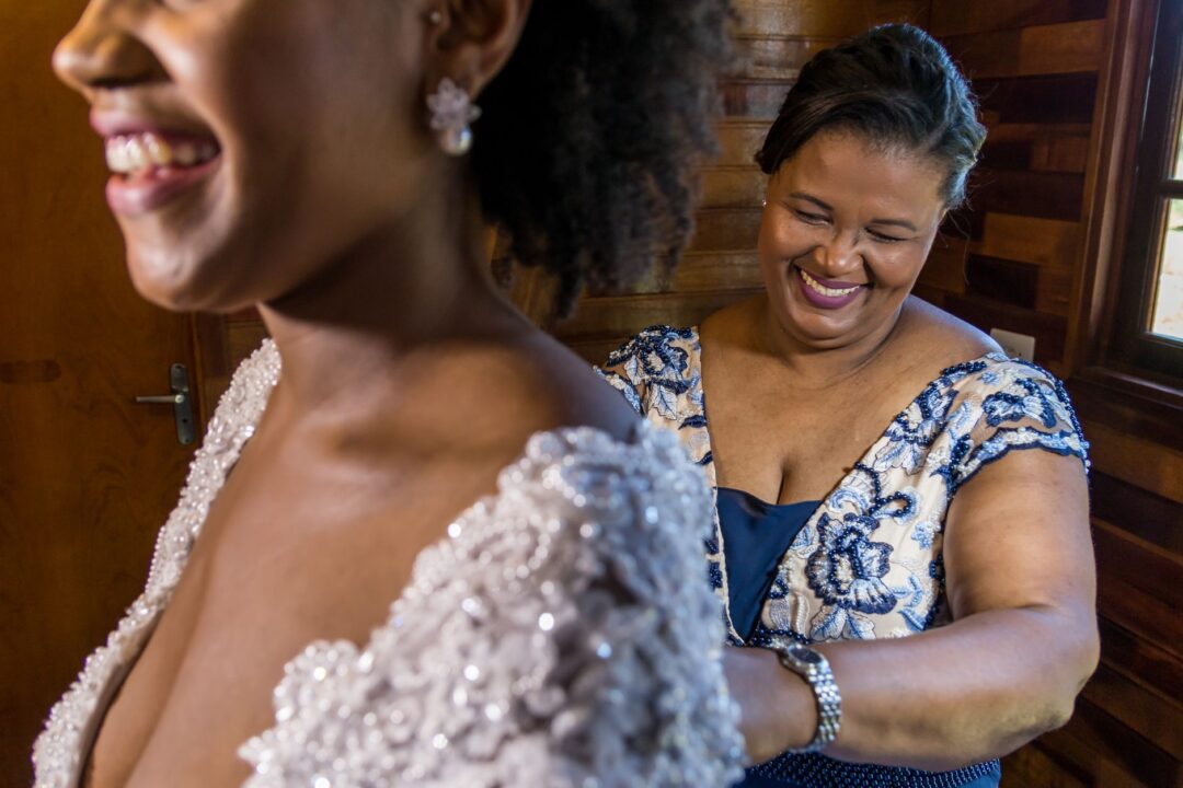 Bride and her mother sharing a warm, candid moment in a cozy bridal boutique lounge, the bride seated in her gown with a...