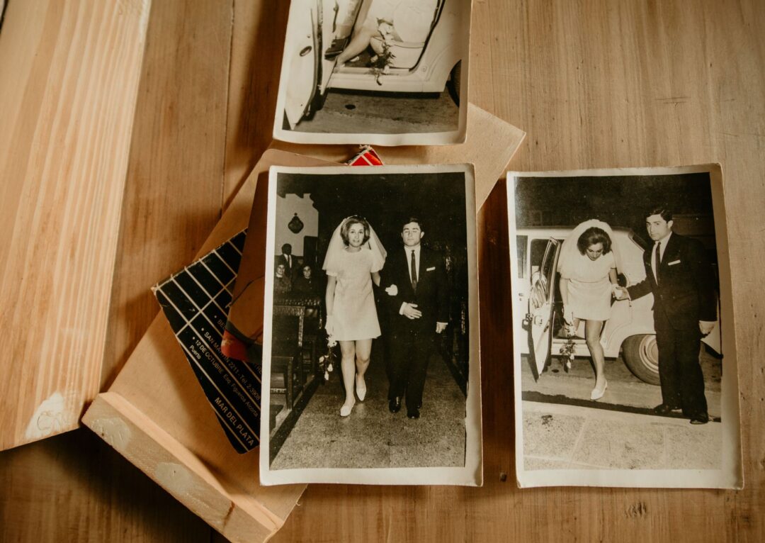 Wedding photographer's flat lay showing an open heirloom photo album with ceremony images, a USB drive in a cloth pouch,...
