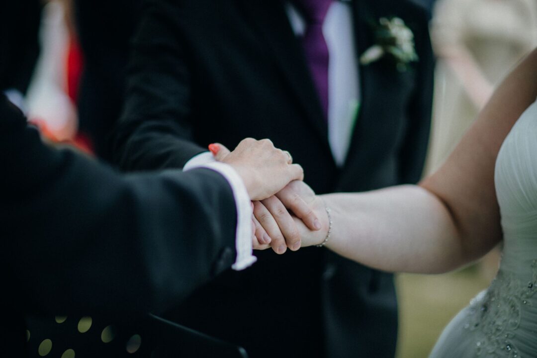 Close-up of a bride and groom exchanging vows outdoors with a professional wedding photographer in soft focus in the...