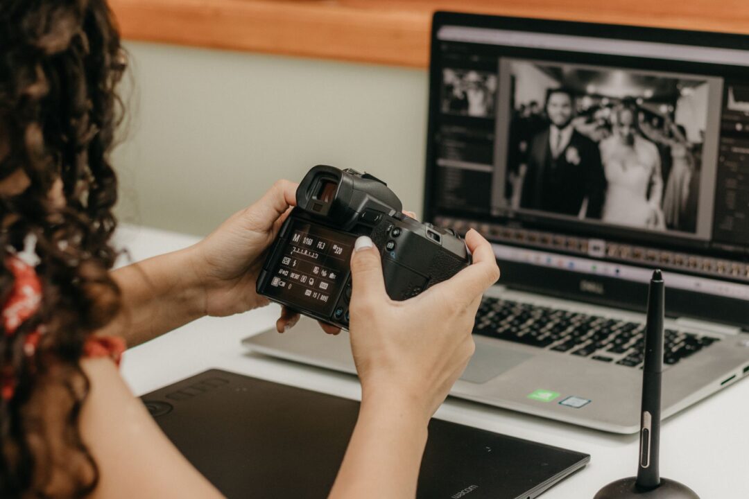 Couple reviewing their wedding photo gallery on a laptop with their photographer at a bright studio consultation table,...