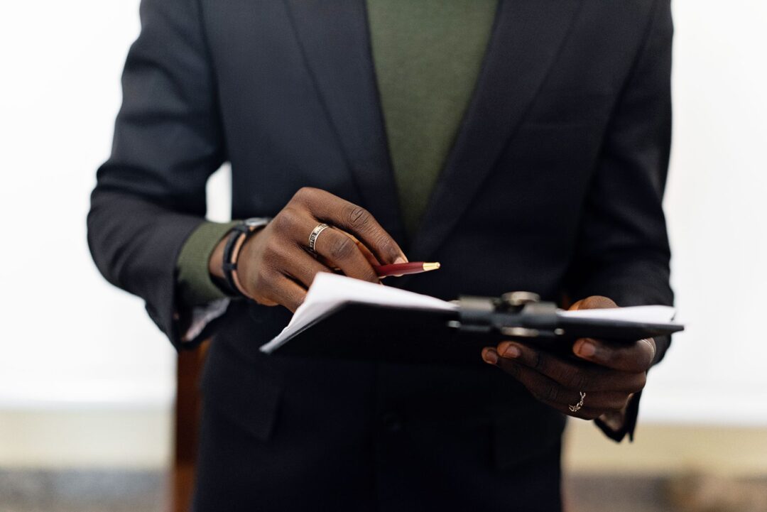 Wedding coordinator in a blazer checking off vendor arrivals on a clipboard while flower arrangements are delivered to a...