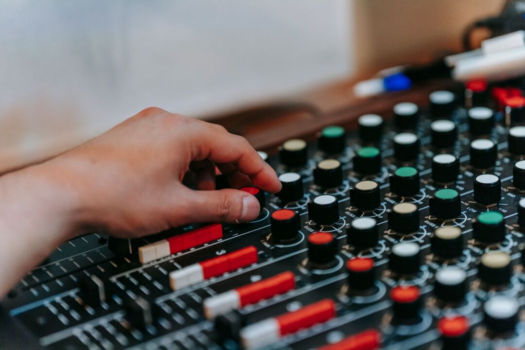 Sound technician adjusting levels on a digital mixing board at an outdoor wedding reception, warm evening light with...