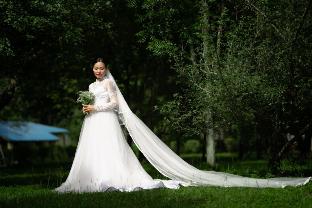 Bride in a simple ivory gown seen from behind, wearing a long cathedral-length soft tulle veil trailing across polished...
