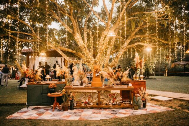 Elegant outdoor wedding reception at golden hour with string lights overhead, round tables draped in white linen, and...