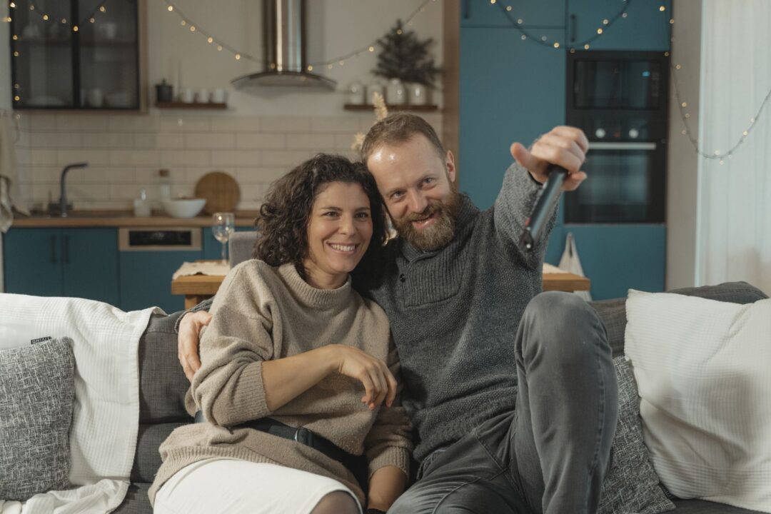 Smiling couple sitting together on a couch watching their wedding highlight film on a laptop