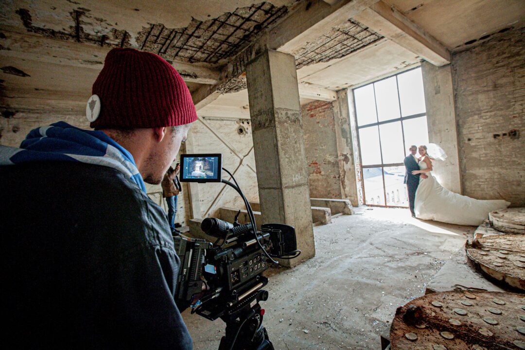 Professional wedding videographer filming a bride and groom's first dance in a warmly lit ballroom reception