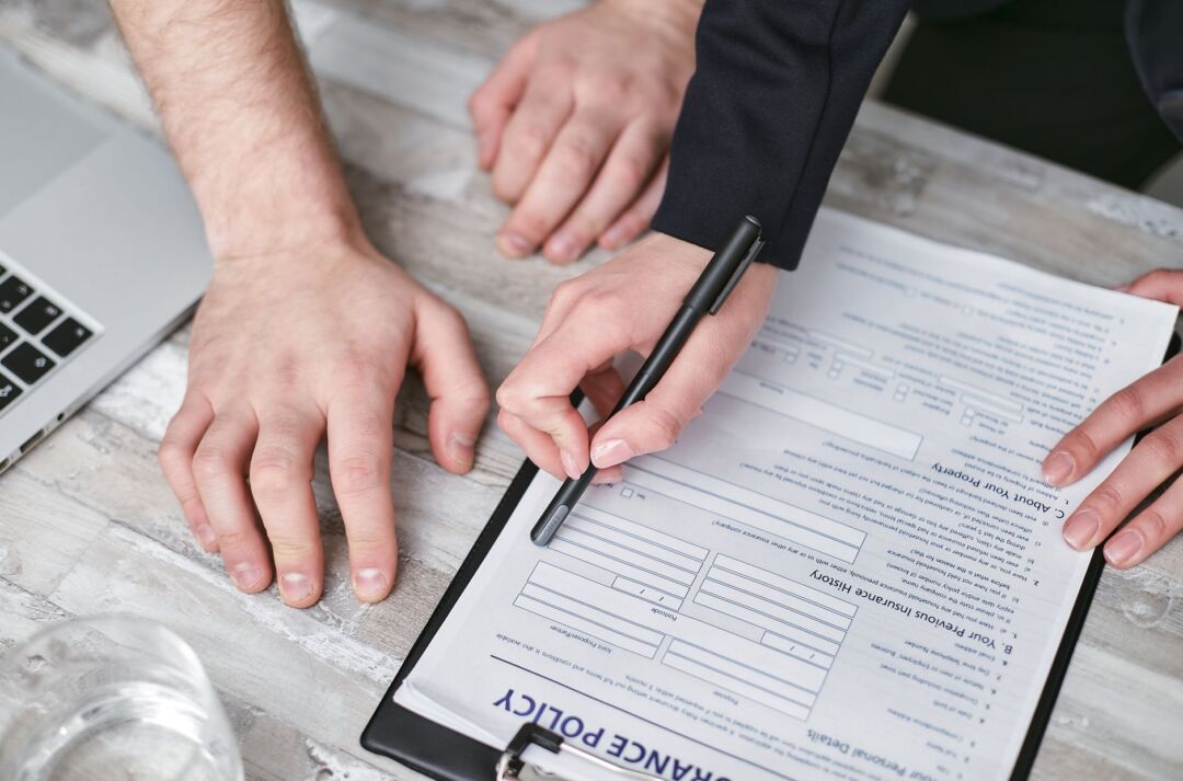 Wedding insurance policy document and a pen resting on a desk beside a small arrangement of white flowers, clean and...