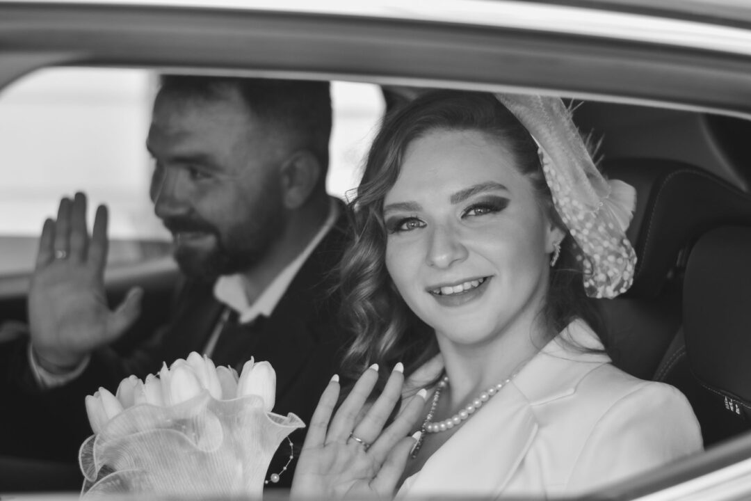 Bride and groom waving from inside their wedding car