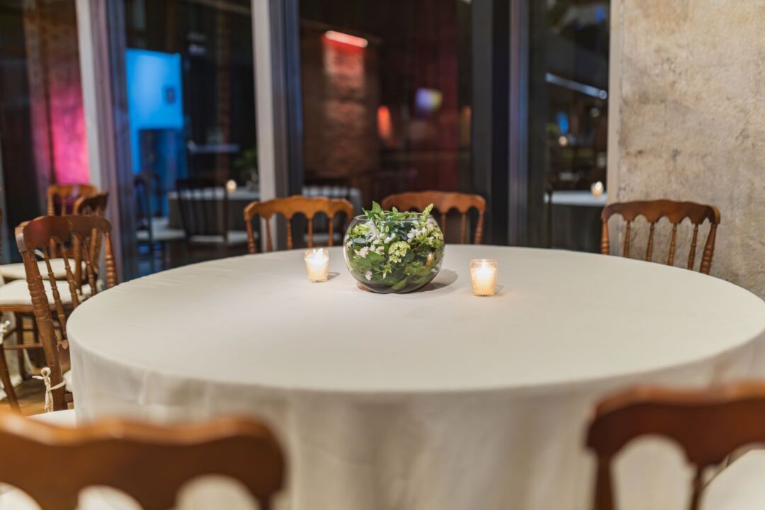Intimate evening reception in progress with round tables set with candles and white florals, guests in formal attire,...