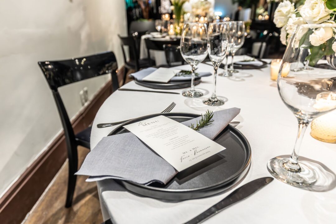 Bright indoor engagement party at a restaurant private dining room, with an elegantly set long table, florals in tall...