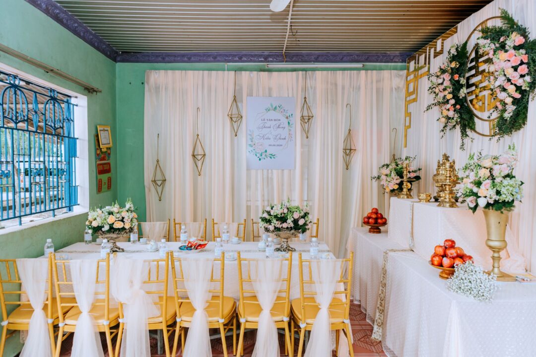 Cozy home engagement party setup with a gallery of engagement photos on the wall, balloons in ivory and sage, and guests...