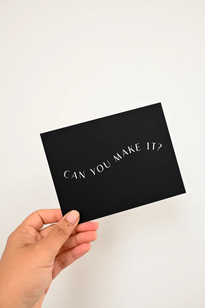 Paperlust All We Need Is Love RSVP card in black, held in hand, printed with the curved line can you make it question